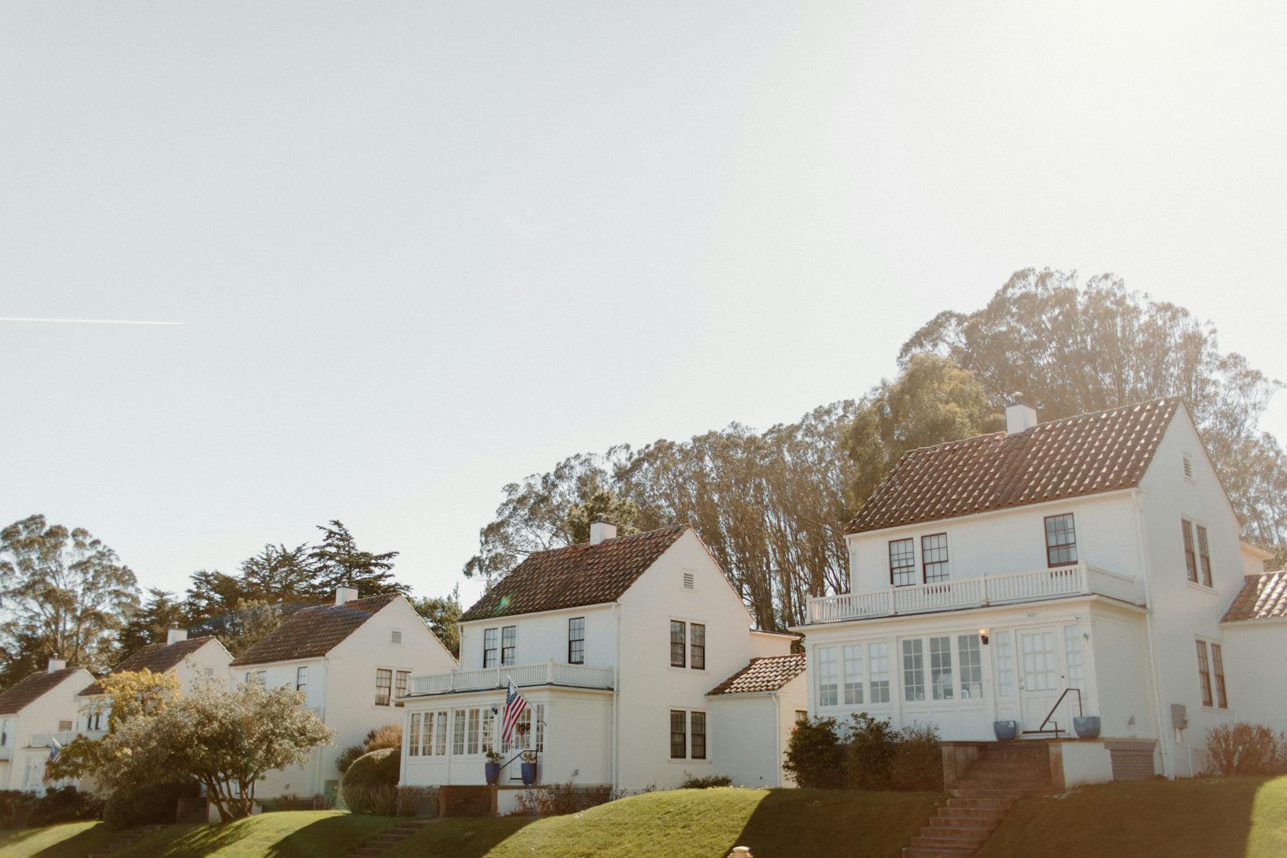 Sunlit view of classic white row houses in a green San Francisco neighborhood.